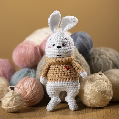 Picture of crochet white long-eared bunny wearing
                blue crochet overalls next to a baby.