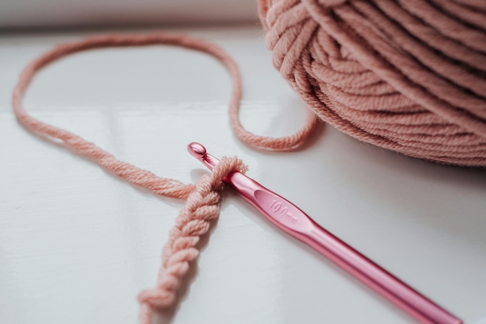 A crochet hook making chain stitches with a pink 3-4mm yarn.