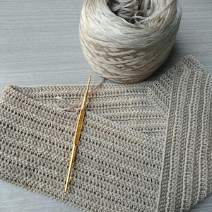Picture of in progress gray scarf that's 
                folded in a triangle shape with the crochet hook in the middle of stitches 
                with a ball of gray thin yarn.