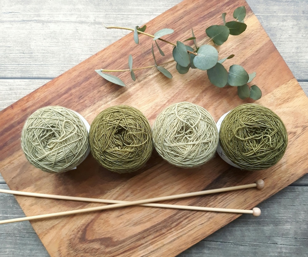 A wooden board with four cakes of different green colored yarn.